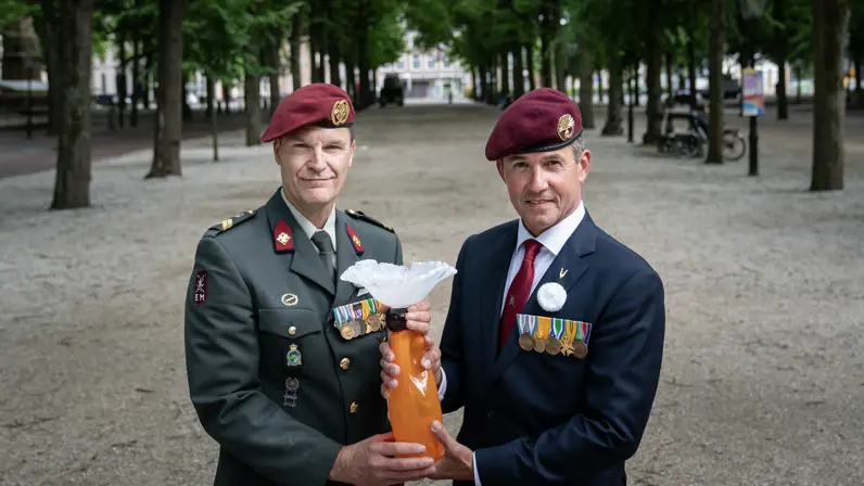 Twee militairen houden een beeld van een witte anjer vast. 
