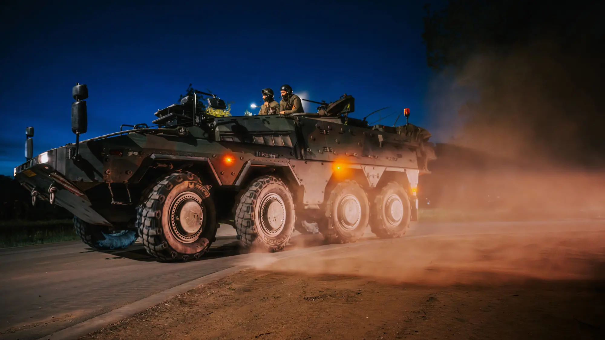 Militairen rijden in pantservoertuig over stoffige weg bij duisternis.