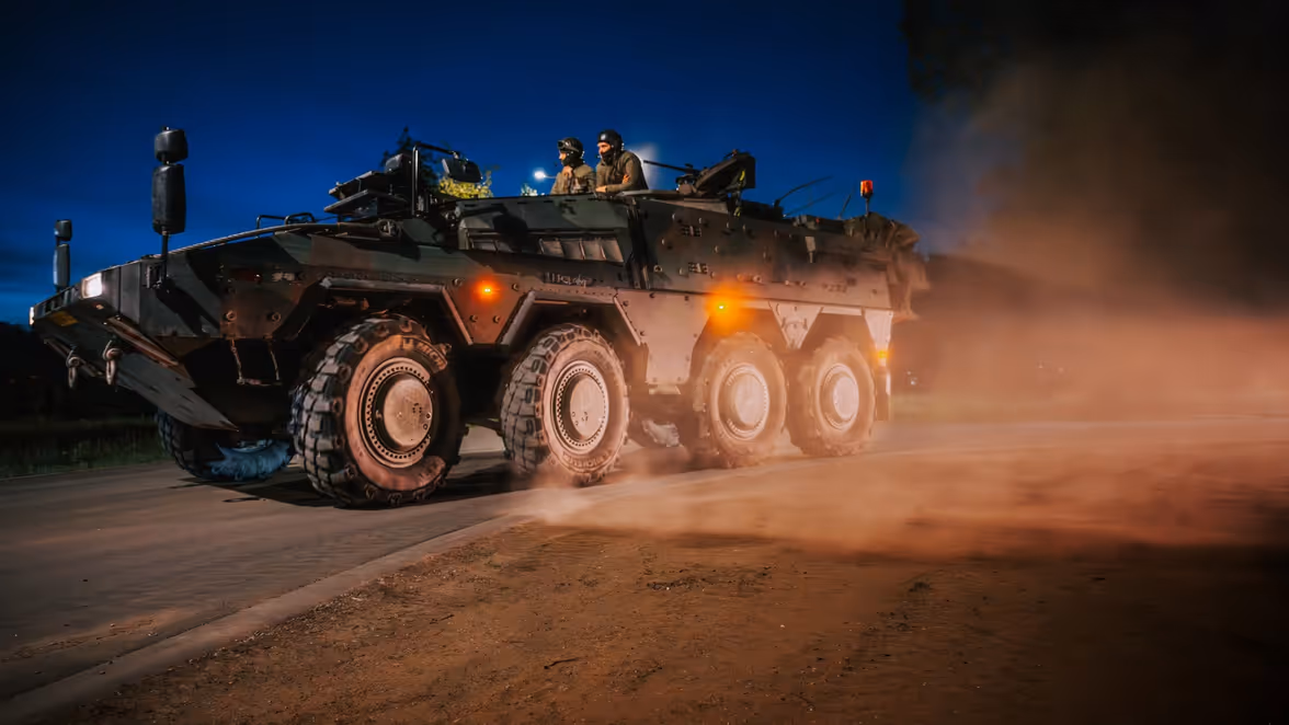 Militairen rijden in pantservoertuig over stoffige weg bij duisternis.