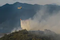 Chinook-helikopter die water uit een oranje bambi bucket laat vallen op brandend terrein.