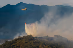 Chinook-helikopter die water uit een oranje bambi bucket laat vallen op brandend terrein.