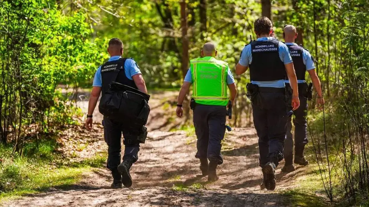 Vier marechaussees op de rug gezien, lopen door de natuur.