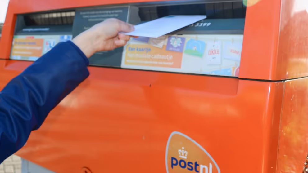 Iemand stopt een brief in een brievenbus.