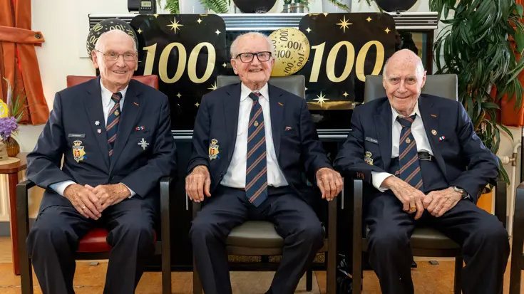 Drie 100-jarige veteranen zitten gemoedelijk naast elkaar.