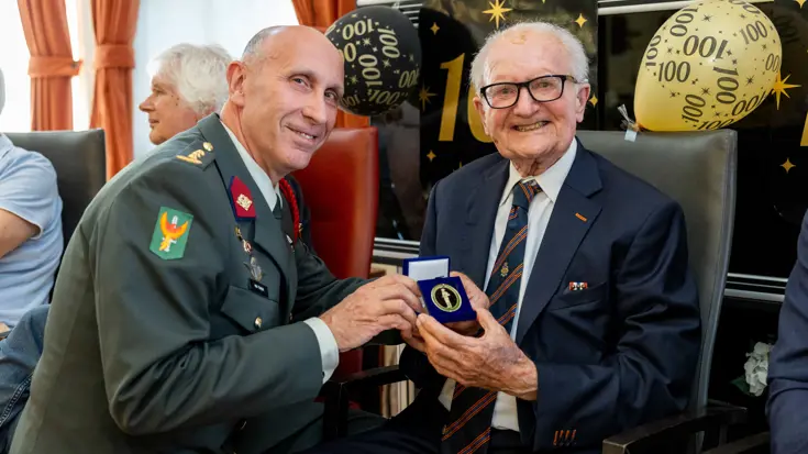 Commandant reikt 100-jarige coin uit.