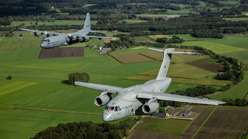Een C-390-transportvliegtuig, rechts in beeld, vliegt naast een C-130 boven Nederlandse weilanden.