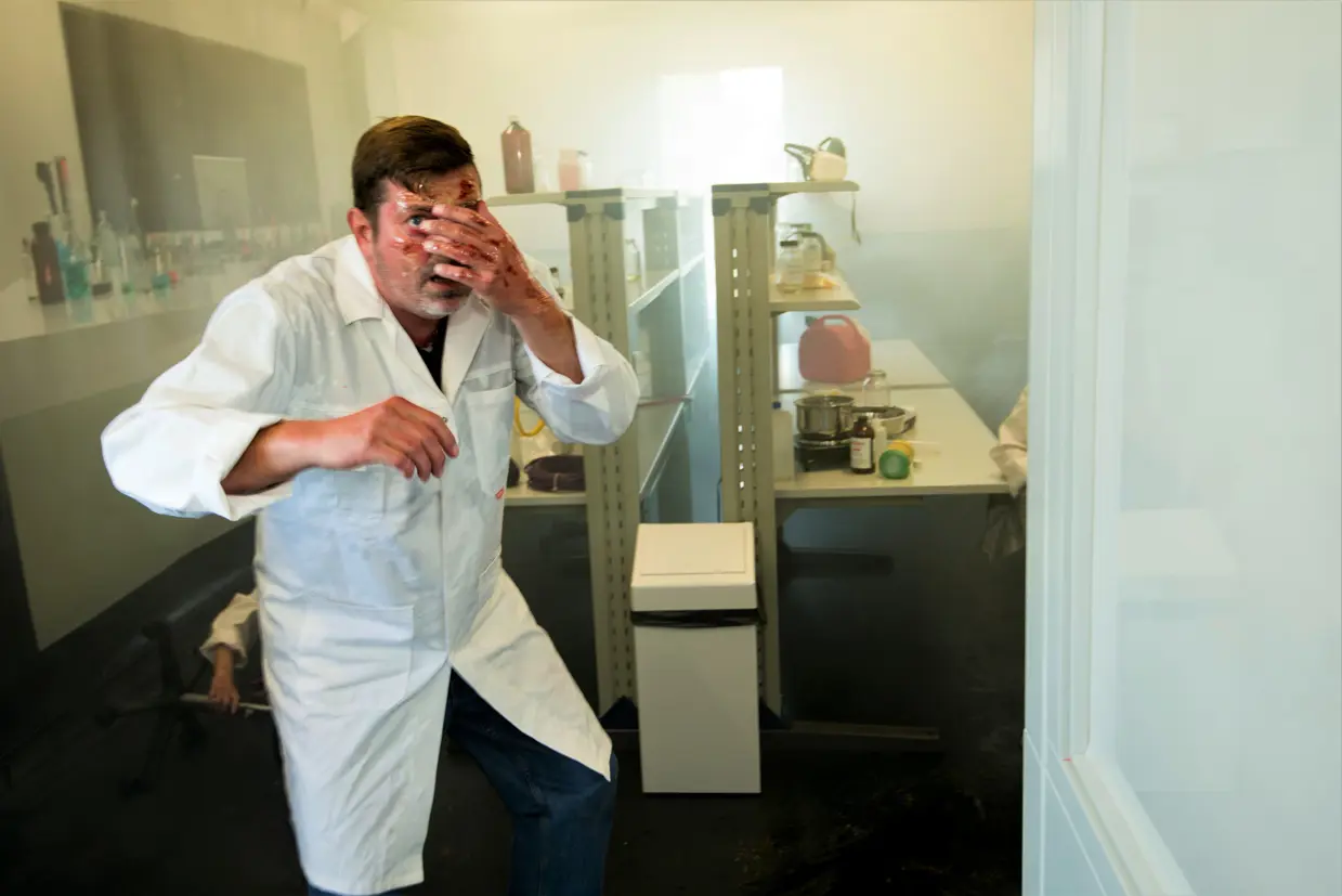 Persoon met brandwonden in gezicht en handen in een Laboratorium.