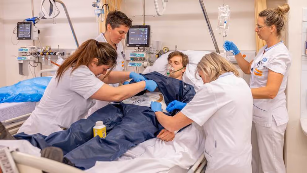 4 zorgmedewerkers behandelen een patiënt die in bed ligt tijdens een oefening.