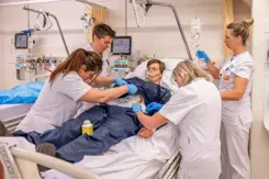 4 zorgmedewerkers behandelen een patiënt die in bed ligt tijdens een oefening.