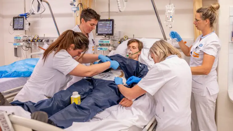 4 zorgmedewerkers behandelen een patiënt die in bed ligt tijdens een oefening.