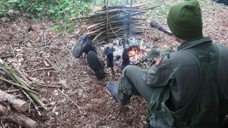Een militair maakt een vuurtje in het bos.