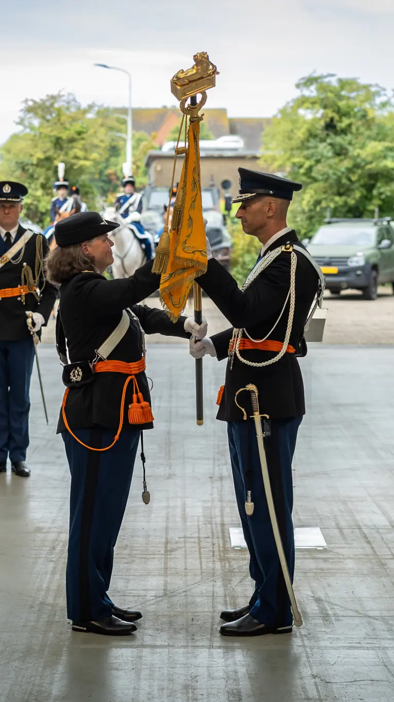 Luitenant-generaal Annelore Roelofs (links) overhandigt de oranje KMar-standaard aan luitenant-generaal Roger Costongs.