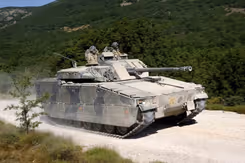 Een CV90 gevechtvoertuig rijdt op een zandpad. Op de achtergrond een groen begroeide heuvelrug.