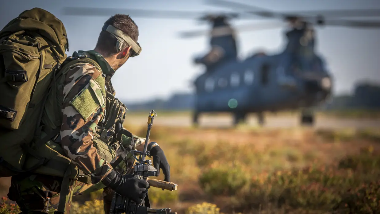 Luchtmobiele militair wacht voordat hij aan boord kan van de Chinook-transporthelikopter op de achtergrond, oefening Hot Blade 2014.