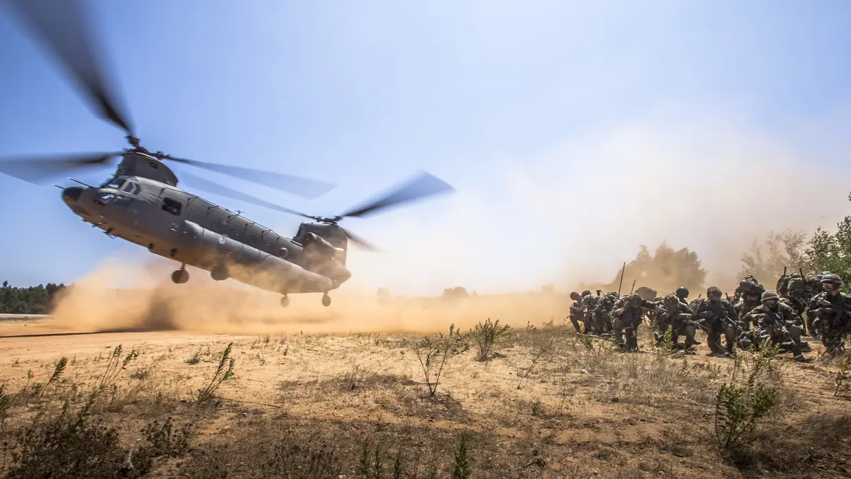 Luchtmobiele militairen groeperen zich terwijl een Chinook-transporthelikopter arriveert voor een volgende dropping.