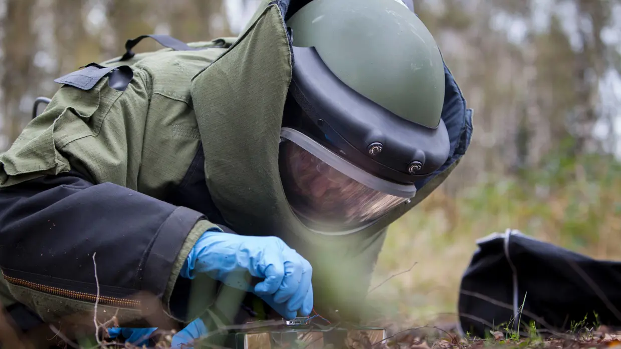 Een explosievenruimer in een bommenpak ontmantelt een oefenexplosief.