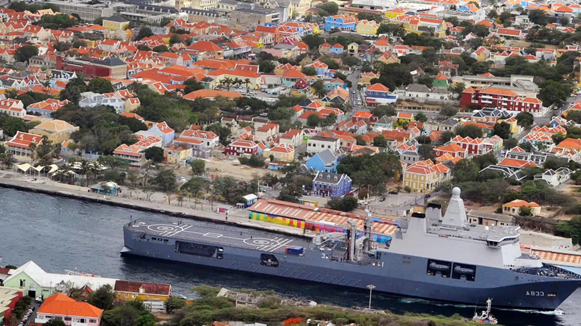 Marineschip vaart door kanaal langs gekleurde huizen.