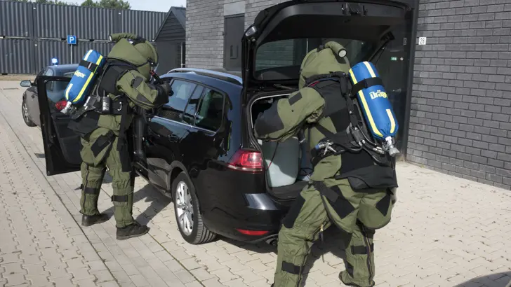 Militairen in beschermende pakken onderzoeken een auto.