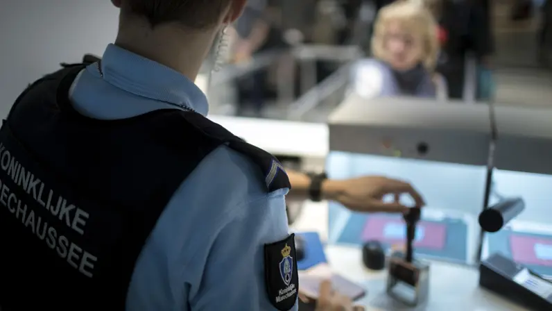 Een lid van de KMar gaat een paspoort stempelen.