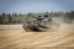 Een CV90 rijdt over een zandvlakte. 