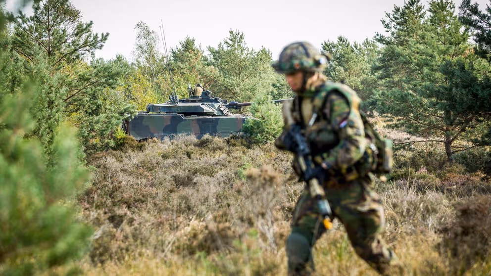 Militair met op de achtergrond een militair voertuig. 