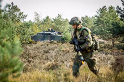 Militair met op de achtergrond een militair voertuig. 