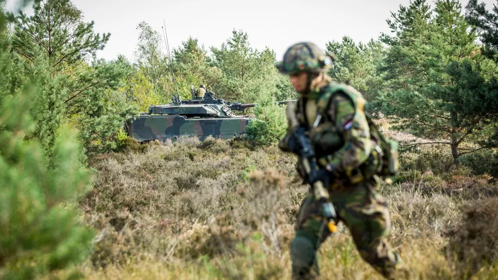 Militair met op de achtergrond een militair voertuig. 