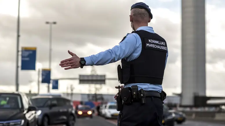 Een marechaussee op de rug gezien, wijst een voertuig naar de controleplaats.