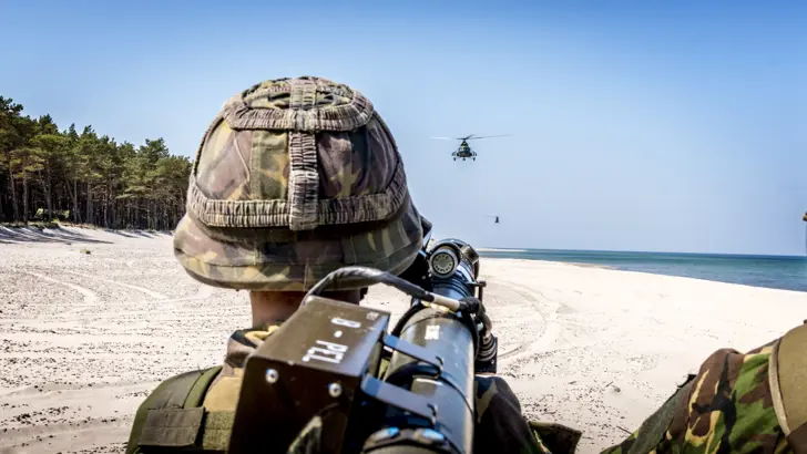 Militair staat op strand en richt stinger-luchtdoelraker op helikopter.