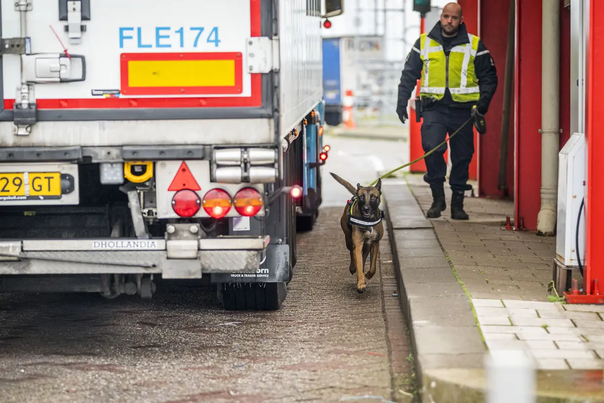 Marechaussee loopt met speurhond langs een vrachtwagen.