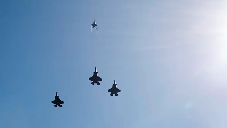 ‘Drie F-35’s vliegen naast elkaar, een vierde exemplaar vliegt recht omhoog. Rechts is de zon te zien.