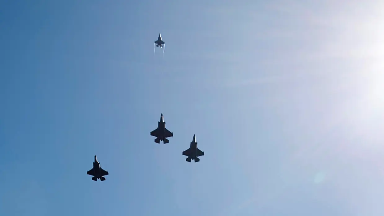 ‘Drie F-35’s vliegen naast elkaar, een vierde exemplaar vliegt recht omhoog. Rechts is de zon te zien.