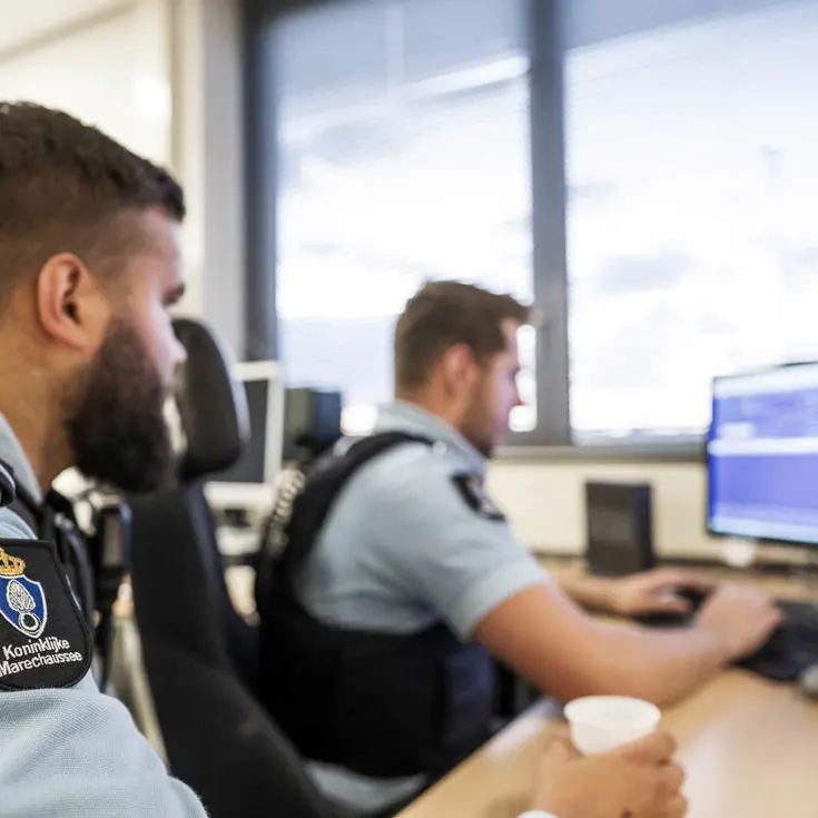 Twee marechaussees kijken naar het PC-scherm.