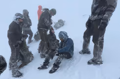 Mariniers staan in de sneeuw om een man heen die op de grond zit en uit een beker drinkt. 