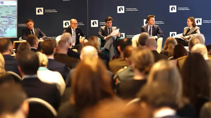 Vier ministers van Defensie zitten naast elkaar tijdens een panel. Op de voorgrond de hoofden van de aanwezigen.