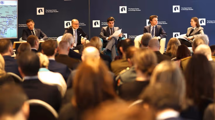 Vier ministers van Defensie zitten naast elkaar tijdens een panel. Op de voorgrond de hoofden van de aanwezigen.