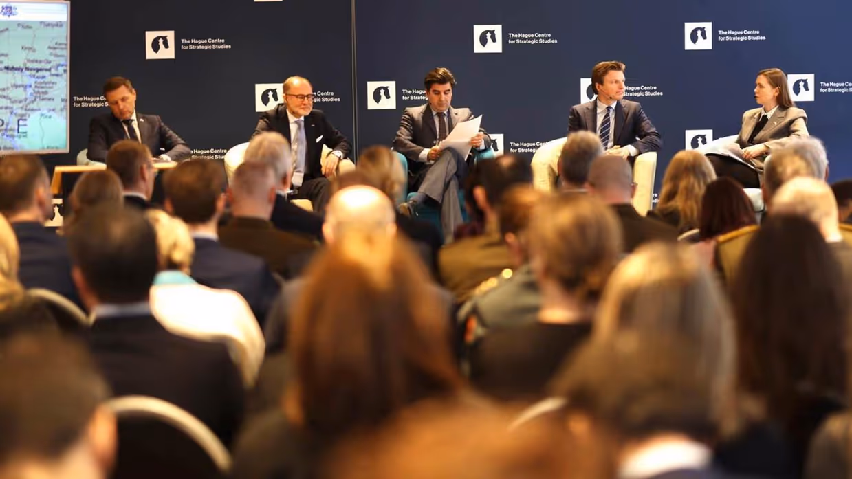 Vier ministers van Defensie zitten naast elkaar tijdens een panel. Op de voorgrond de hoofden van de aanwezigen.