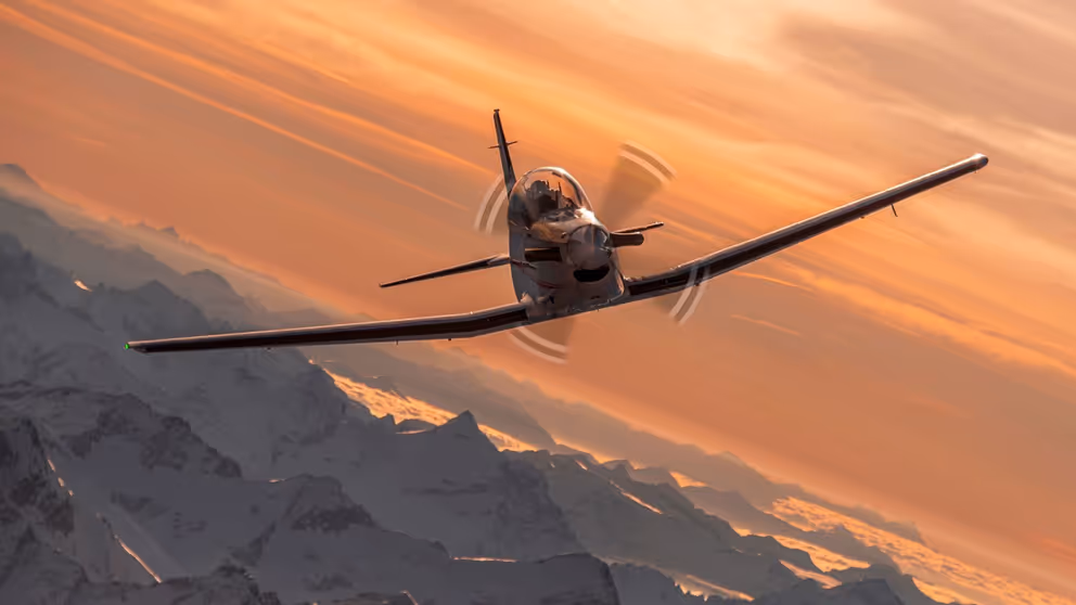 Een PC-7 MKX vliegt in de lucht in een bergachtige omgeving.