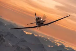 Een PC-7 MKX vliegt in de lucht in een bergachtige omgeving.