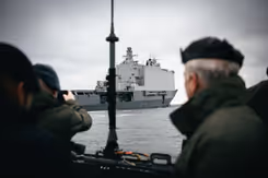 Doorkijk naar Zr.Ms. Johan de Witt op het water. Op de voorgrond een paal en een militair.
