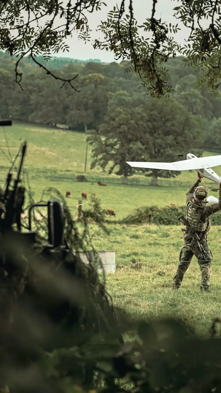 Een militair werpt een drone vooruit in een grasveld.