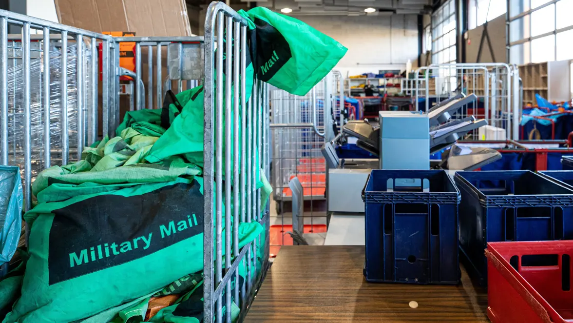 Een militaire postkamer met een rolcontainer en plastic bakken.