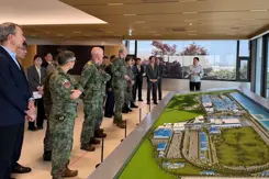 Militairen en burgers kijken naar een groene maquette.