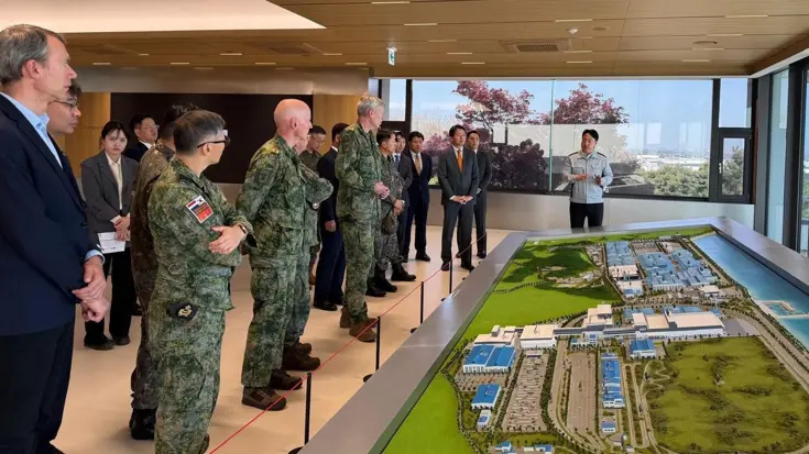 Militairen en burgers kijken naar een groene maquette.