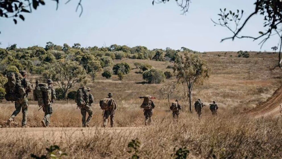 Militairen met bepakking lopen in een rij door natuurgebied.