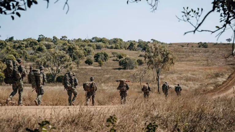 Militairen met bepakking lopen in een rij door natuurgebied.