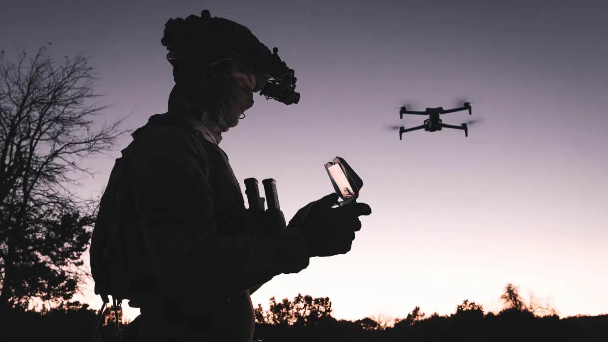 Militair bestuurt drone bij zonsondergang.