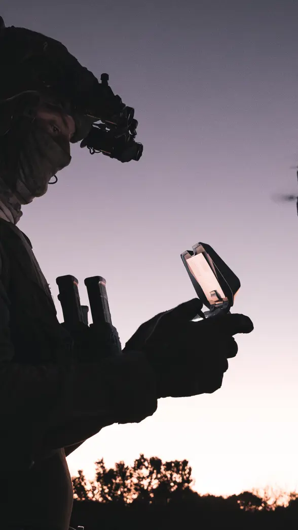 Militair bestuurt drone bij zonsondergang.