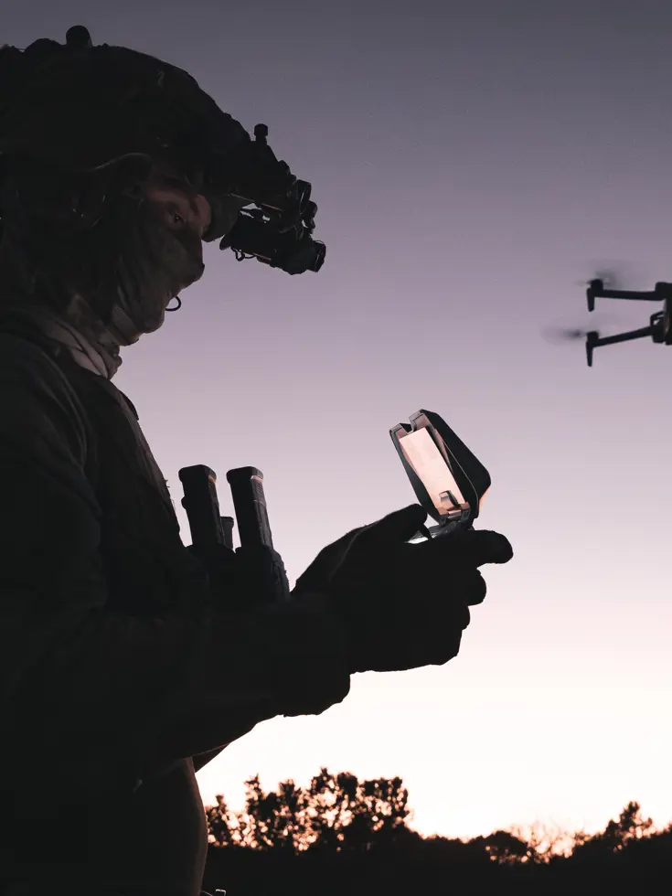 Militair bestuurt drone bij zonsondergang.