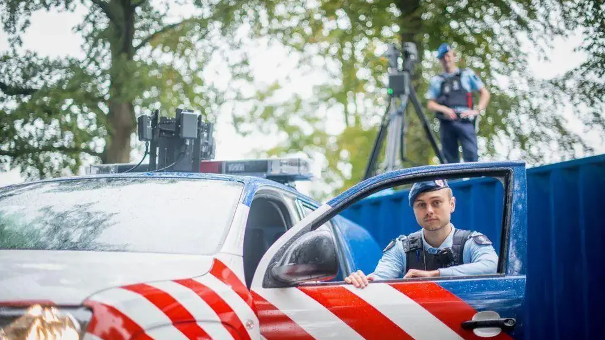 Twee marechaussees poseren bij hun auto en op een container vanaf waar ze drones besturen.